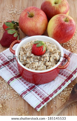 Oatmeal in red bowl with apples and strawberries on wooden block