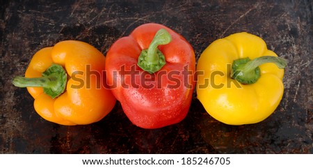 Three sweet peppers (orange, red and yellow) on brown background