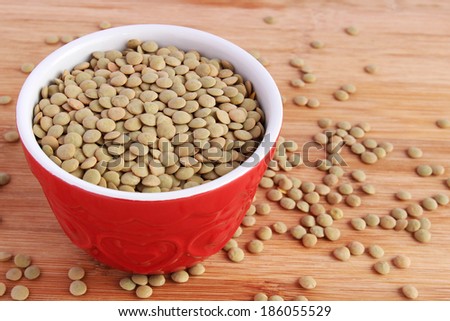 Dry green lentils in red bowl on wooden board