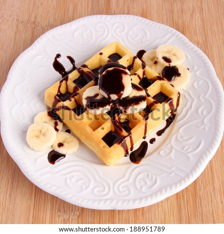 Banana chocolate waffle in white plate on wooden board
