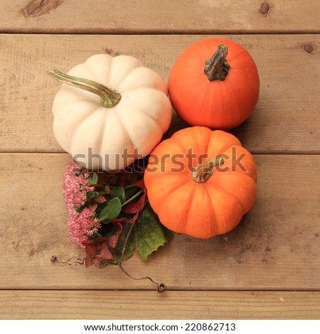 Three pumpkins on wood background with autumn leaves and flowers. Halloween or Thanksgiving decor. Halloween or Thanksgiving decor.