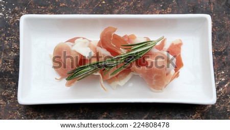 Prosciutto and rosemary in a white plate on brown rustic background