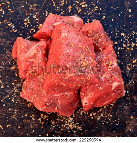 Raw beef cubes with beefsteak spices on brown rustic background