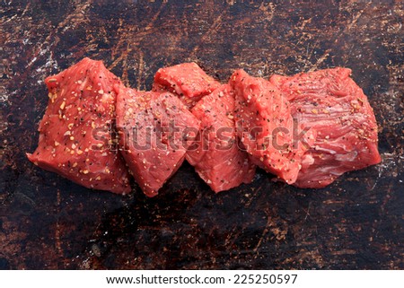 Raw beef cubes with beefsteak spices on brown rustic background