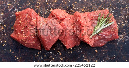 Raw beef cubes with rosemary and beefsteak spices on brown rustic background