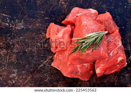 Raw beef cubes with rosemary on brown rustic background
