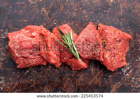 Raw beef cubes with rosemary and beefsteak spices on brown rustic background