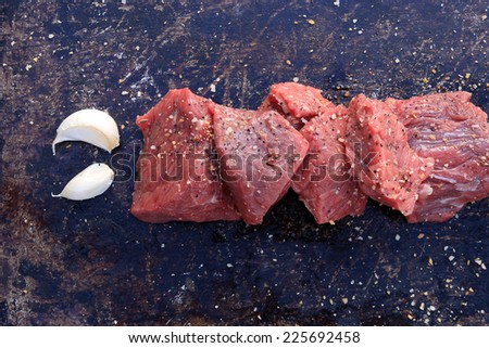 Raw beef cubes with garlic and beefsteak spices on brown rustic background