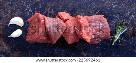 Raw beef cubes with garlic and rosemary on brown rustic background
