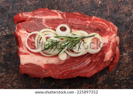 Raw blade roast with onions and rosemary on brown rustic background