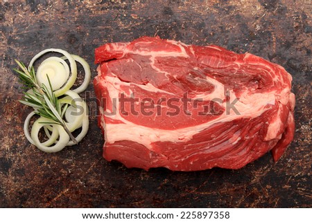 Raw blade roast with onions and rosemary on brown rustic background