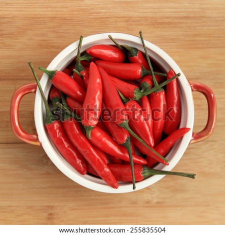 Red thai chili peppers in red bowl on wood background