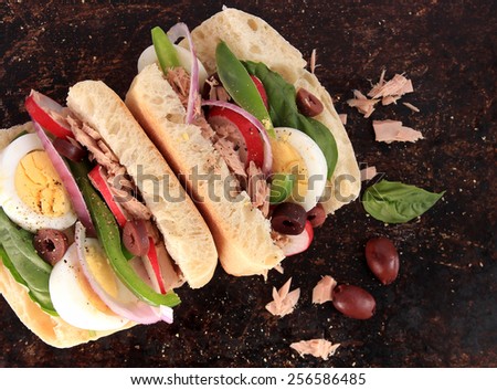 Tuna nicoise sandwich, also known as pan bagnat, on brown rustic background
