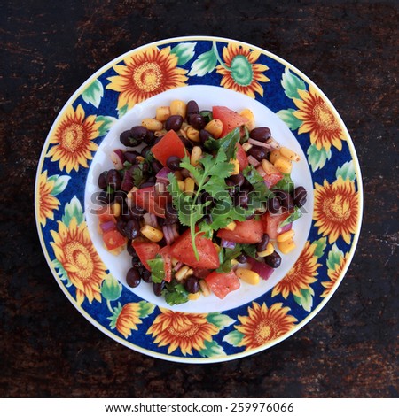 Black bean salad in sunflower plate on brown rustic background