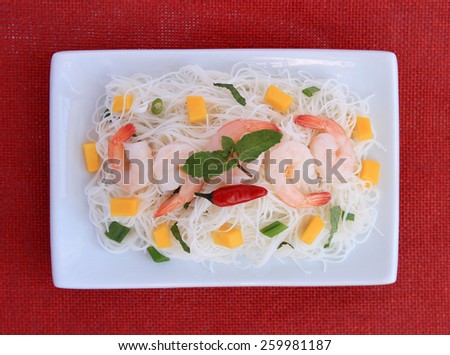 Rice vermicelli, shrimp, mango, green onions and mint in white plate, on red place mat