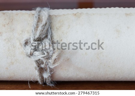 Old scroll paper on wooden background. Close up of rope.