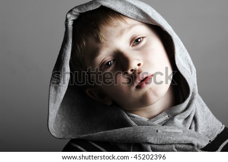 a relaxed little boy in a cool pose with a hoodie gazes on in a low key dramatic setting