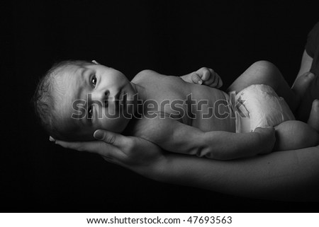 a newly born child gazes at the camera in a low key dramatic setting