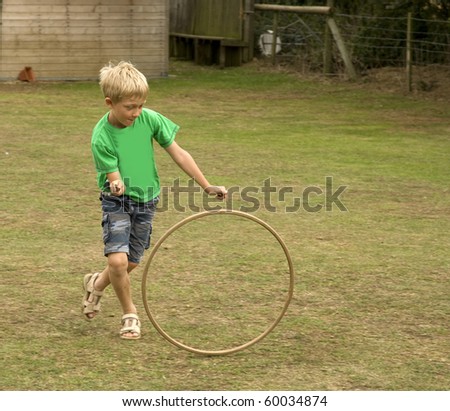 young blonde boy plays with a traditional wooden hoop and stick