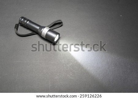 Glowing metal flashlight with wrist strap on a dark background