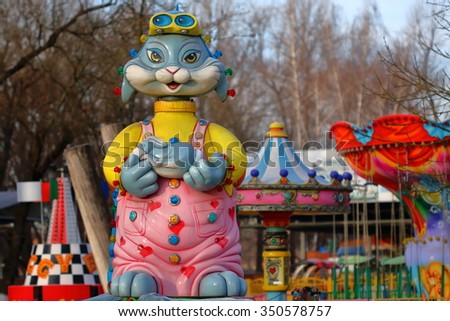 Pyatigorsk, Russia - December 12, 2015: Funny female cat in pink dress keeps in paws a blue rabbit. Detail of the children carousel in City Park.