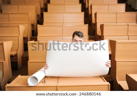 The student in large audience, sitting at a school desk, prepares for examination