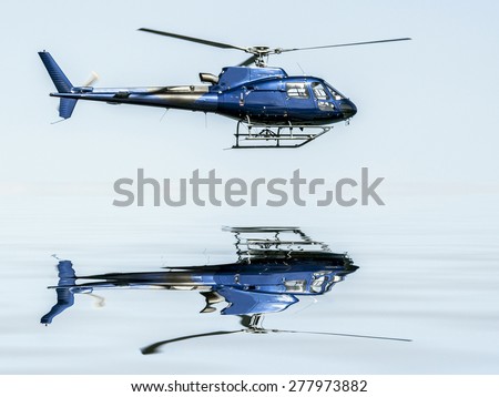 Helicopter flying on blue sky, and reflection in the water