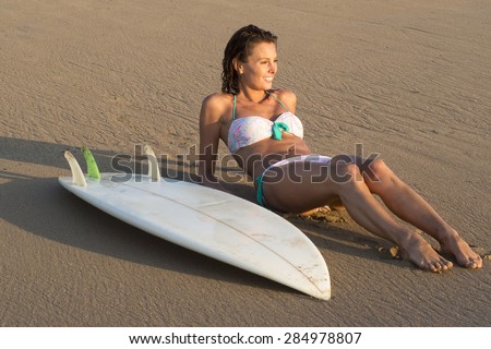 Girl sunbathing on sand beach with surfboard next