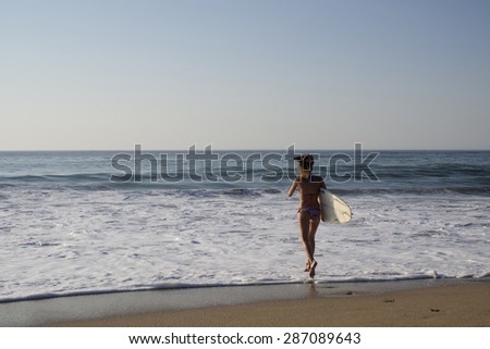 Blonde surfer girl run in bikini on the beach to the sea with a surf board, surfing, footprints on the sand