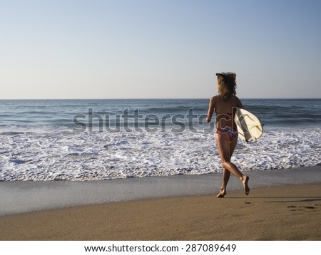 Blonde surfer girl run in bikini on the beach to the sea with a surf board, surfing