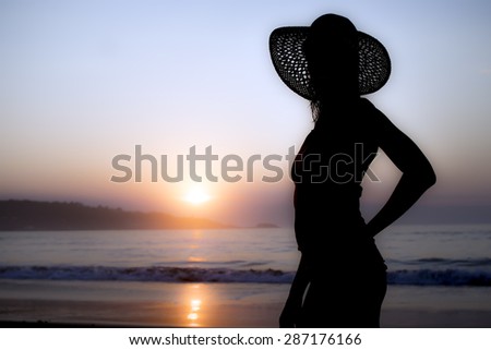 silhouette of fashion slim woman with hat at sunrise on the beach, defocused background