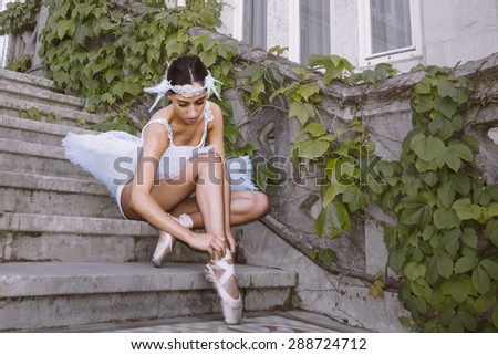 Last settings of pretty ballerina on white tutu, at palace entrance stairs, adjusting their ballet slippers. very cute photography