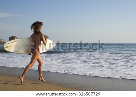 Blonde surfer girl run in bikini on the beach to the sea with a surf board, surfing