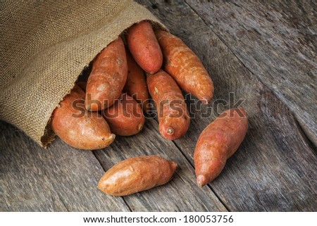 Freshly harvested organic sweet potatoes spilling from a burlap bag onto a natural weathered wood table.