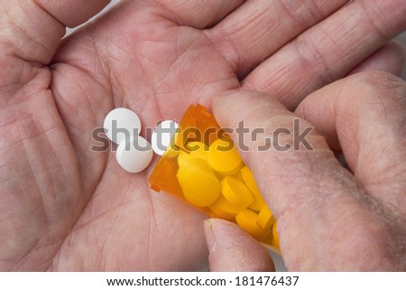 Rough dry hand of a senior man pouring white tablets from medicine bottle into palm of other hand. Focus on pills.