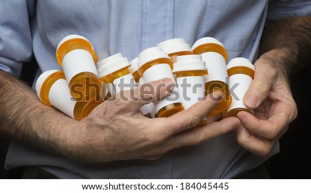 Tight shot of a senior man with rough, dry, hands holding several prescription medication bottles against mid-section.