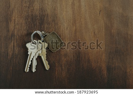 Key chain with three house or door keys on a dark wood table top.
