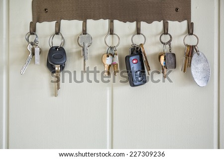 Door, house, and car keys hanging on hooks on a wall.