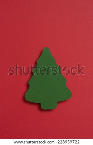 A Christmas tree shape cut from a sheet of green paper floating above a sheet of red.