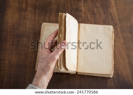 Hand turning blank pages of a vintage book. Shallow depth of field with focus on thumb, fingers and page edges.