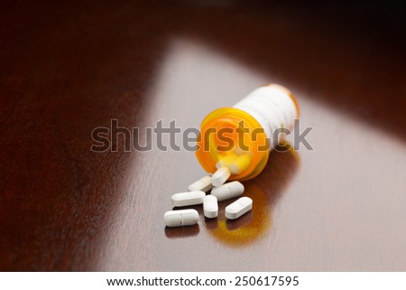 White caplets spilled from an orange medicine bottle onto a table. Shallow depth to field.