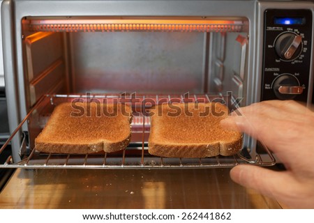 Hand reaching, with motion blur, for slices of whole wheat toast on the rack of a toaster oven from an eye level point of view.