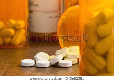 Prescription painkillers, oxycodone, spilled from a bottle onto a table with out of focus\
bottles.