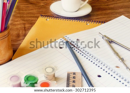 notebooks and pencils, paints, compass, ruler, a cup of coffee on a wooden table