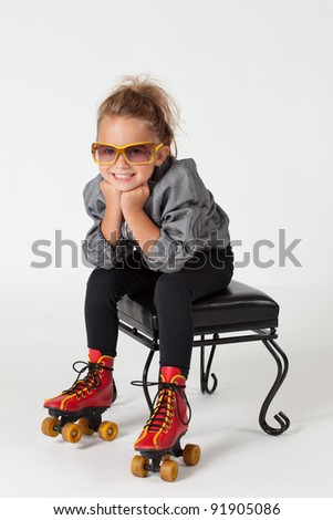 Adorable young girl with roller skates on, sitting on stool on a white background.
