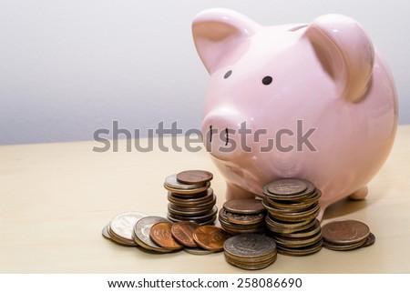 A close-up of a pink piggy bank on the right side of the frame with various coins stacked in front.