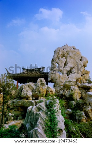 A chinese traditional building on artistic stone hill under blue sky and white cloud.