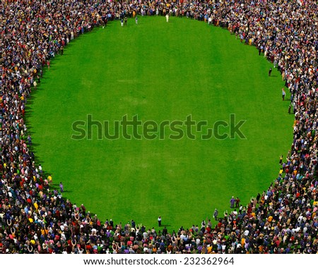 Large group of people seen from above, gathered in the shape of a circle, standing on a green field background