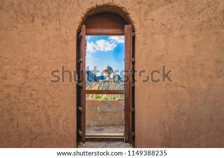 Narrow archway with old, heavy wooden doors opened to show the famous frankincense monument of Muscat, Oman.