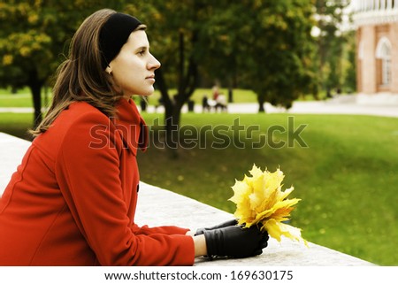 Fall / Autumn woman holding colorful leaves in city park looking forward. Stylish modern portrait of girl holding colorful leaves outdoor in fall park